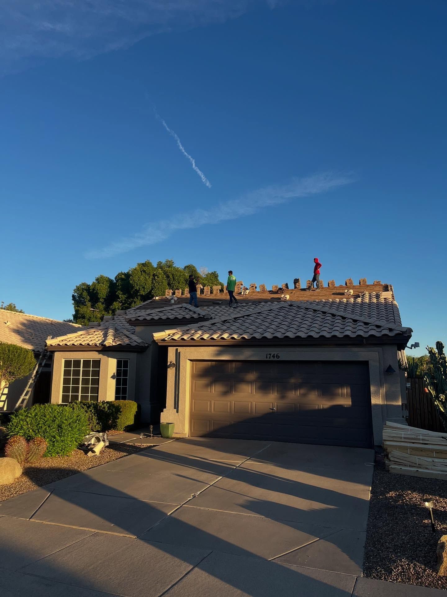A house with roofers working on it, under a blue sky with a contrail.