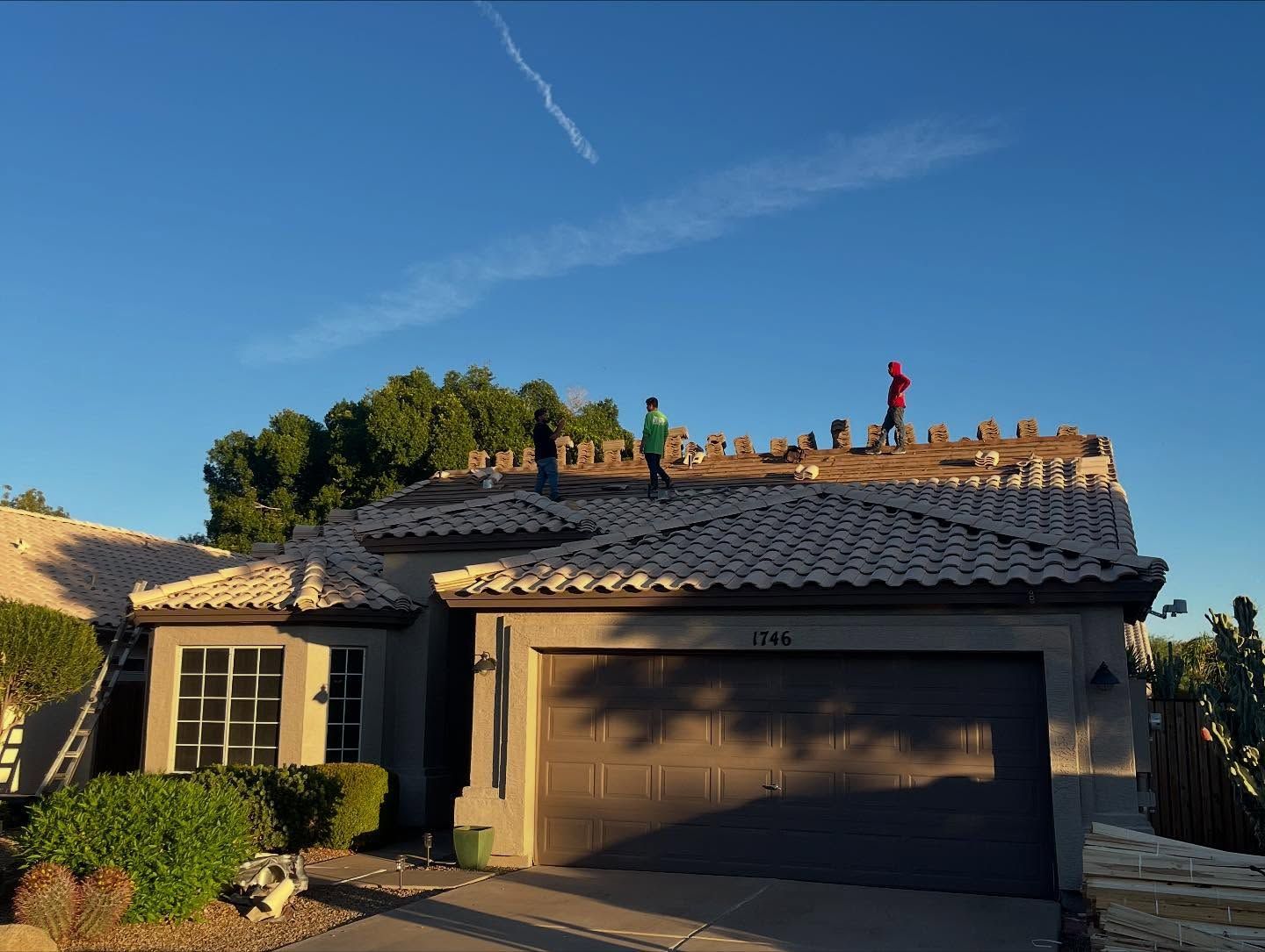Workers installing roof tiles on a house under a clear blue sky.
