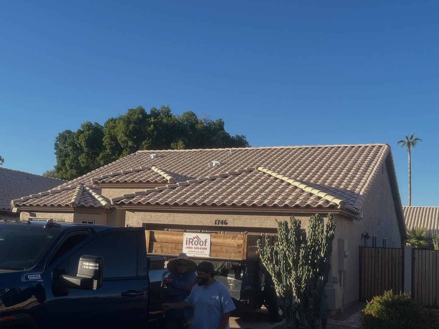 Beige roof tile house with a man near the garage, a dark truck, and a cactus under a clear blue sky.