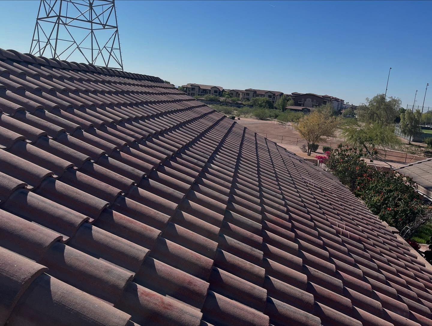 Brown tile roof angled toward a sunny, clear sky, with power lines in the background.
