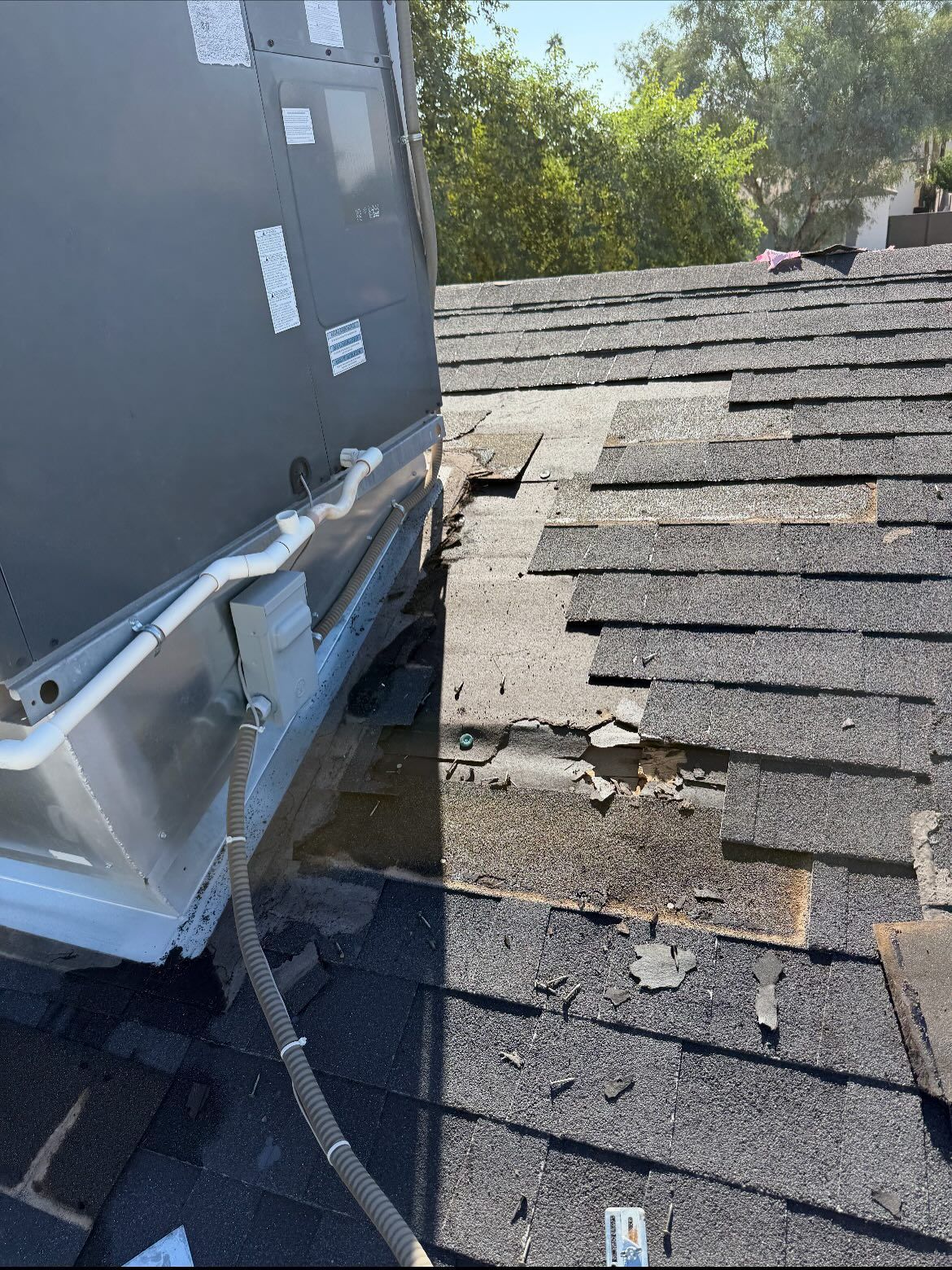 AC unit sits on damaged roof shingles, revealing underlying wood.