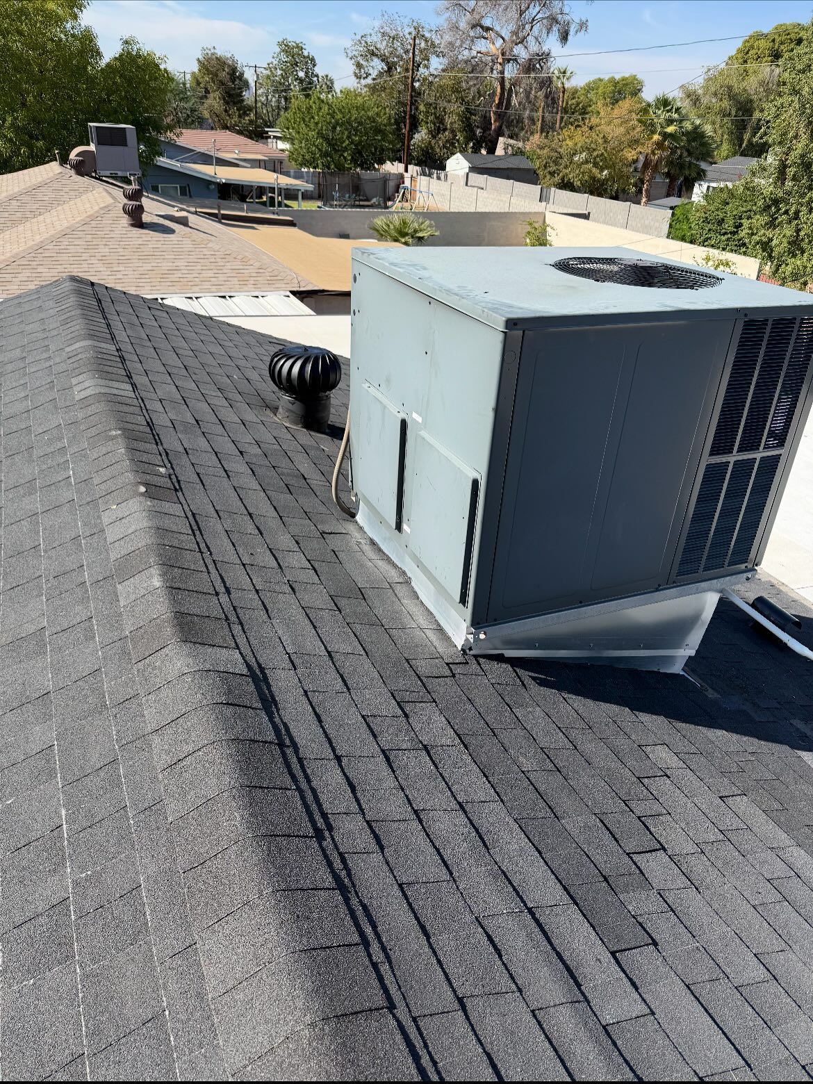 Gray rooftop with HVAC unit and vent. Trees and other houses are in the background.