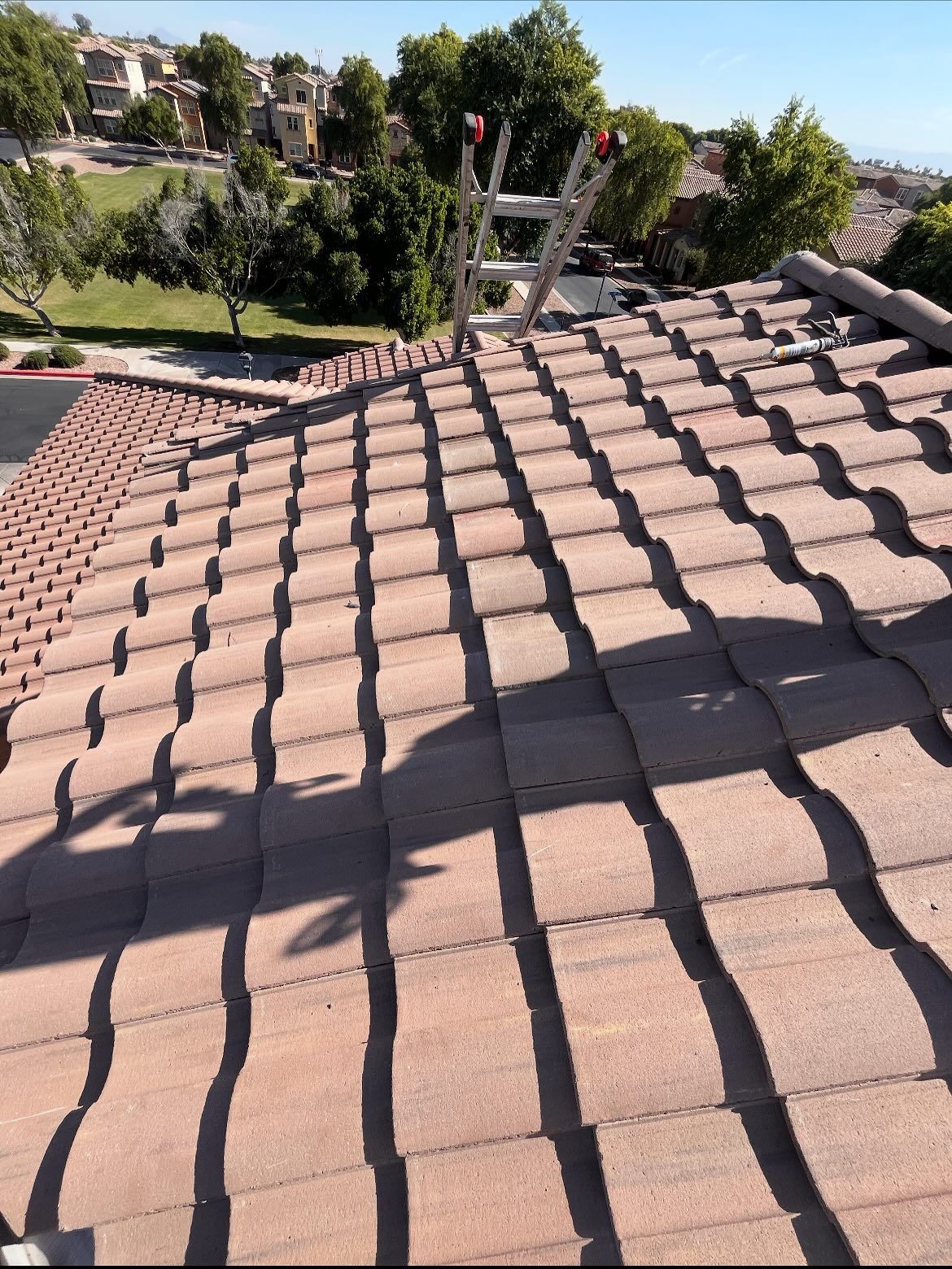 Red tile roof with ladder and shadows cast by sunlight.