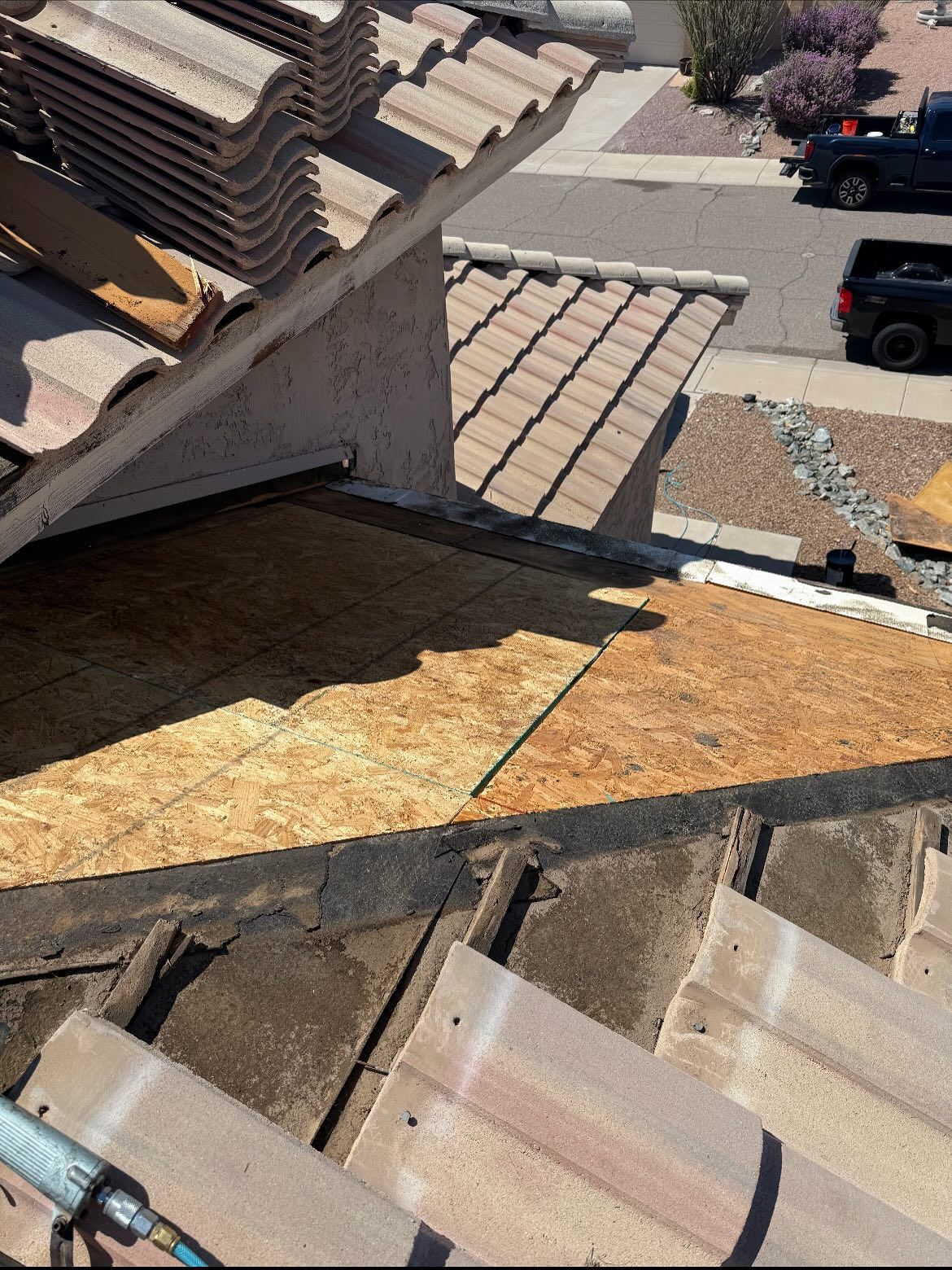 Rooftop repair: exposed plywood, missing tiles, stacks of new tiles, street visible in the background.
