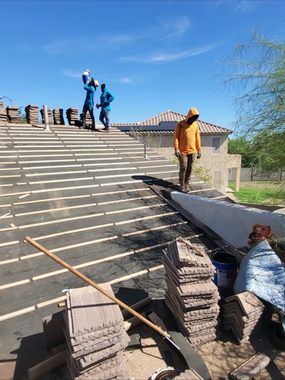 Roofers installing tiles on a residential roof under a blue sky.
