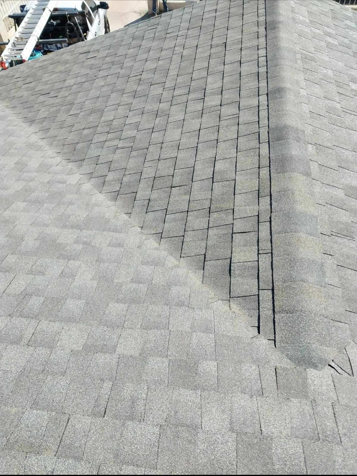 Gray asphalt shingle roof with vertical seam; repair ladder in the background.