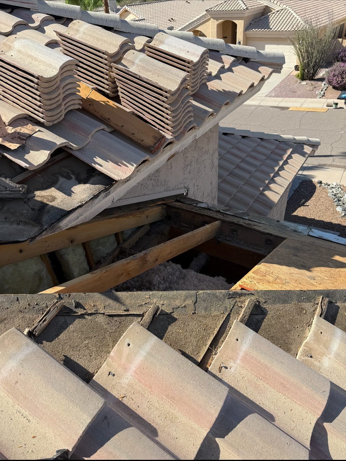 Damaged roof with missing tiles, exposing wooden structure and debris.