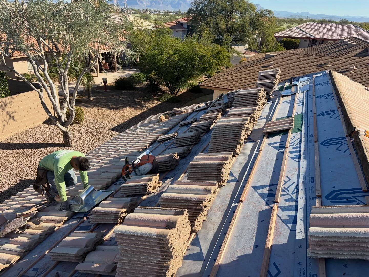 Roofer on a roof replacing tiles. Work in progress, with stacks of tiles and protective underlayment visible.
