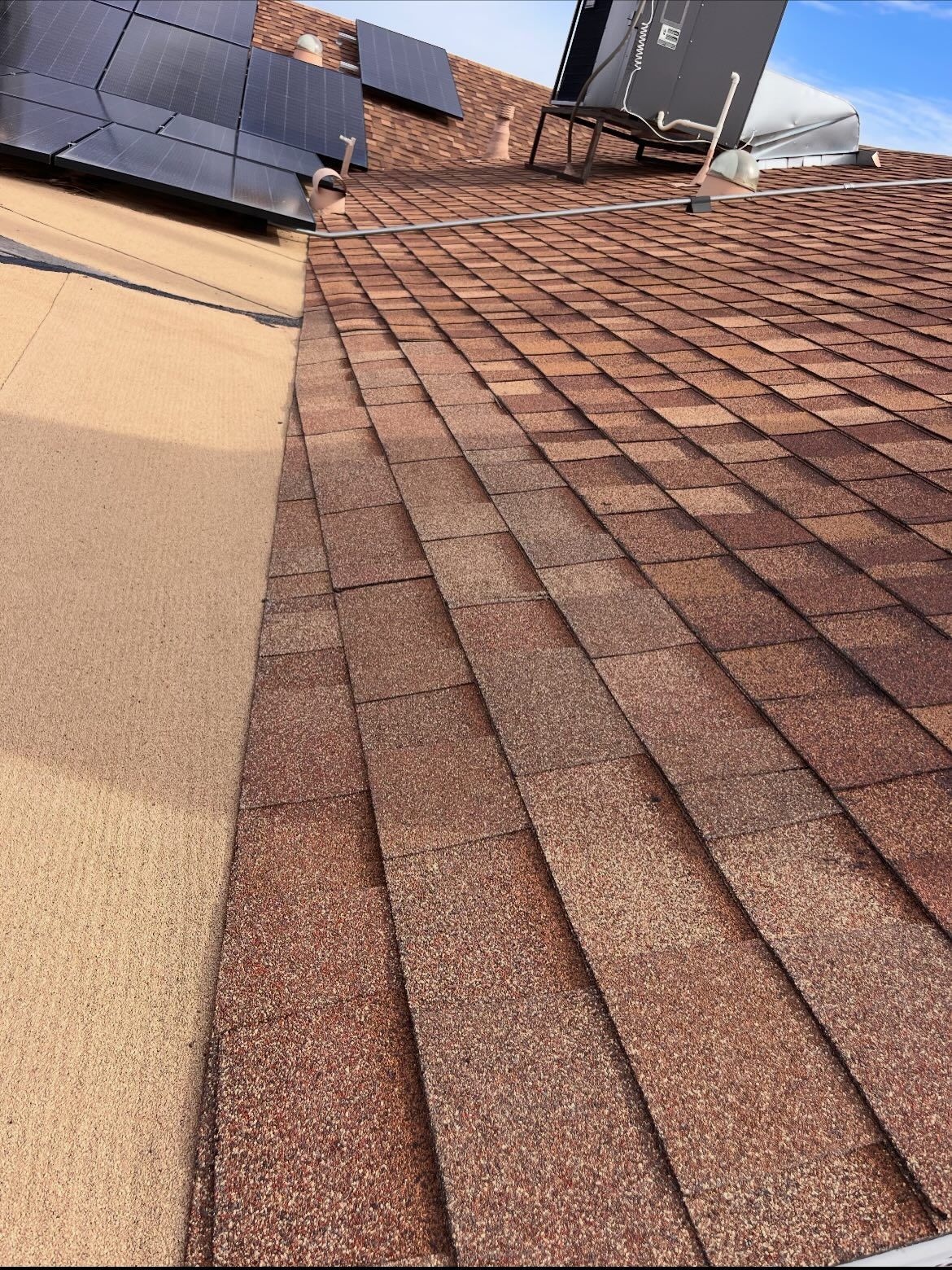 Brown asphalt shingle roof with solar panels. Overhang with tan colored fascia. Bright sky.