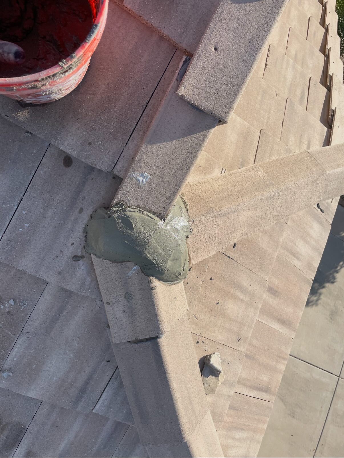 Roof tiles with mortar at an intersection, with a bucket in the corner.