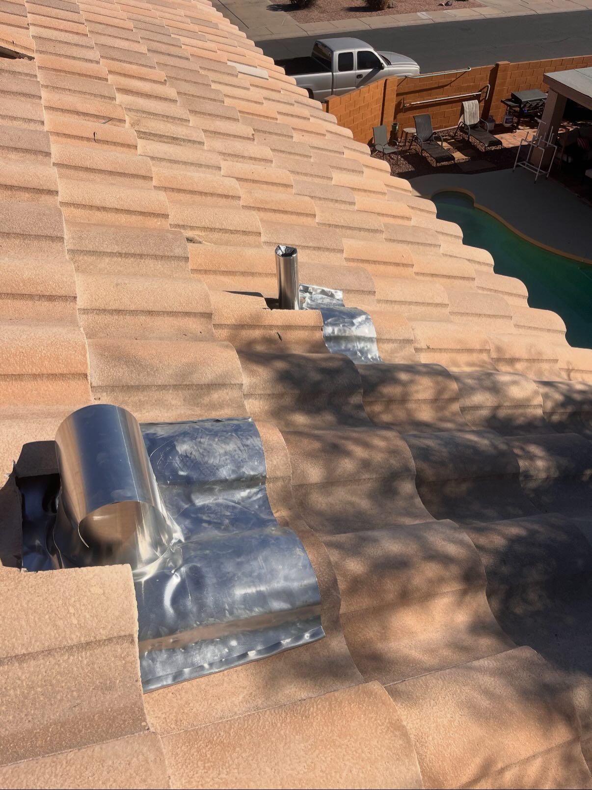 Close-up of a tiled roof showing metallic flashing around two vents.