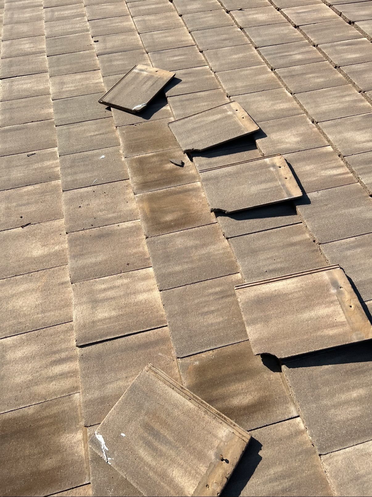 Close-up view of a brown asphalt shingle roof with several displaced shingles.