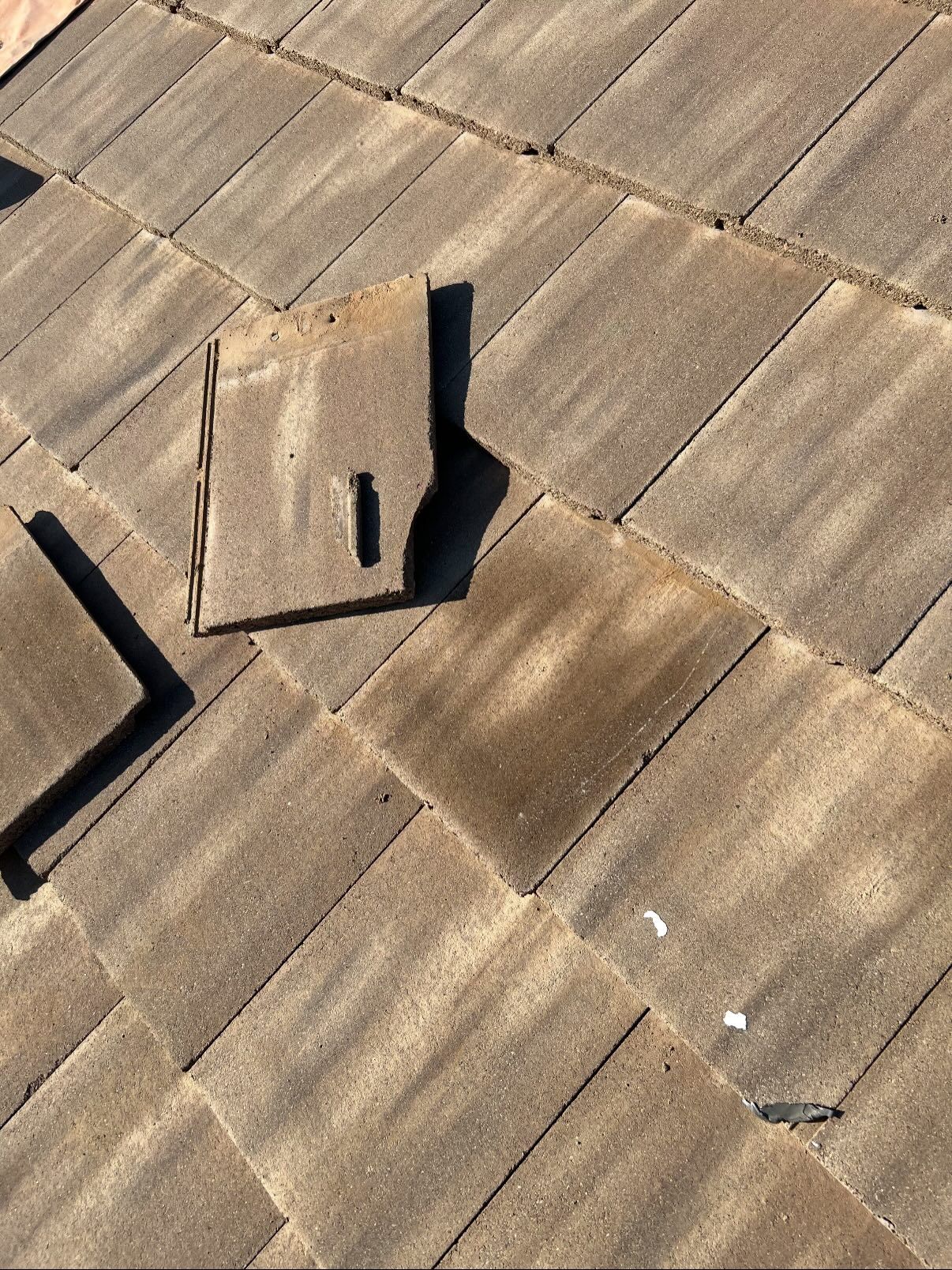 Overhead view of a roof with a missing tile. The replacement tile is laying next to the empty space.