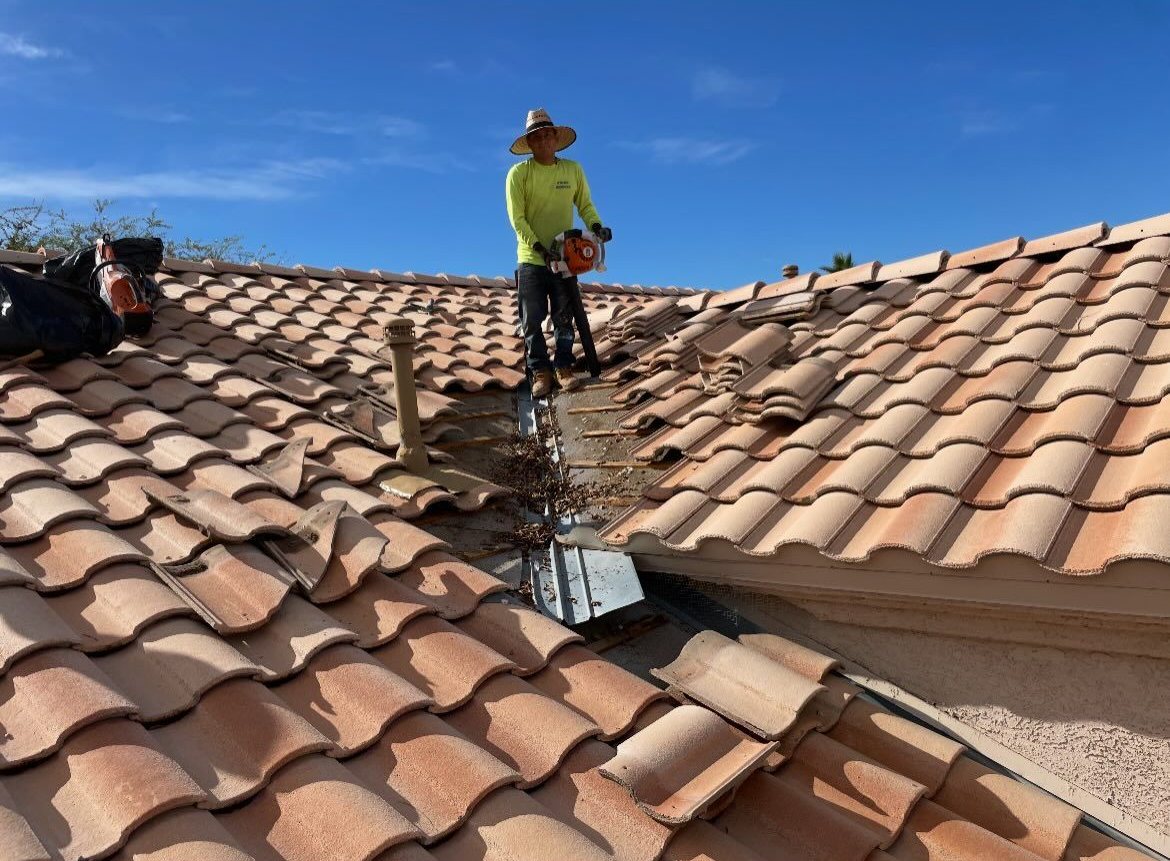 Person on a roof using a saw to cut tiles, likely repairing the roof. Sunny day.