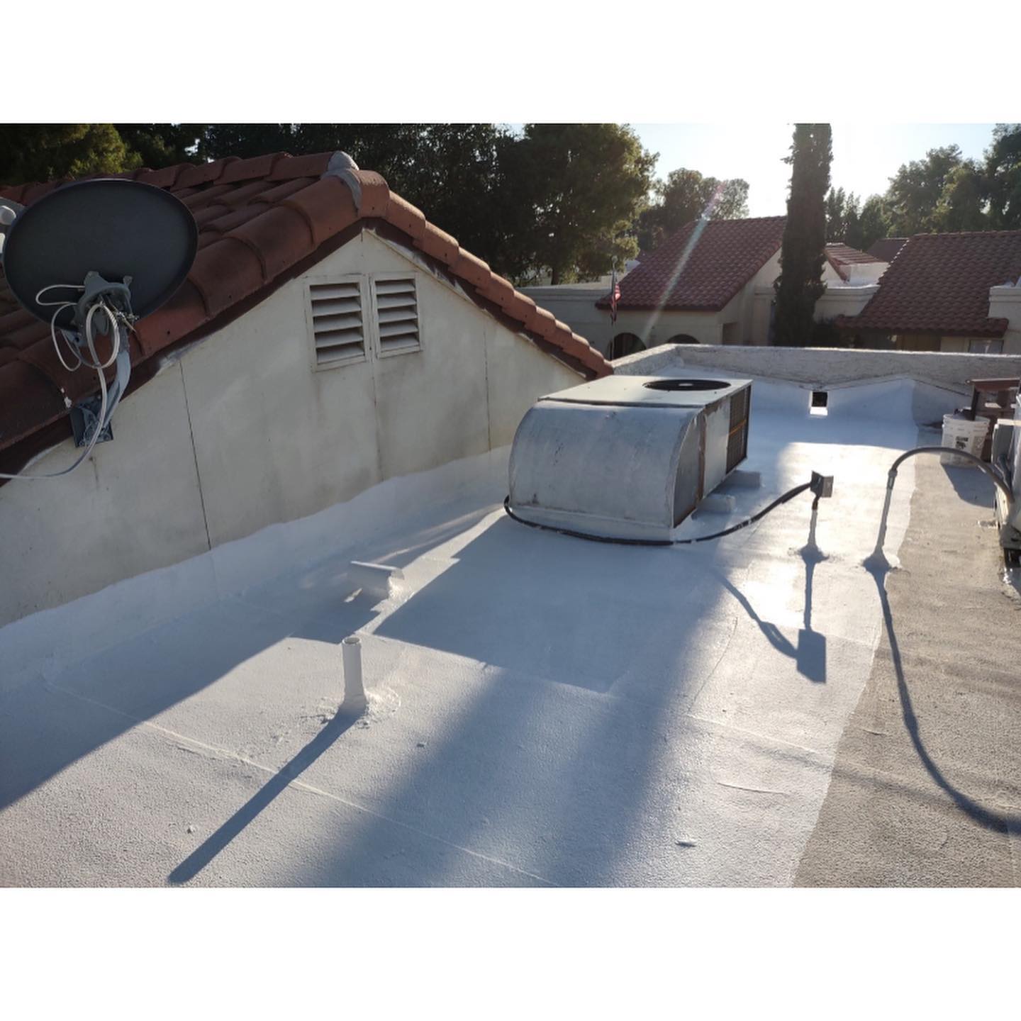 Flat white roof with air conditioning unit, antenna, and adjacent building with red-tile roof.