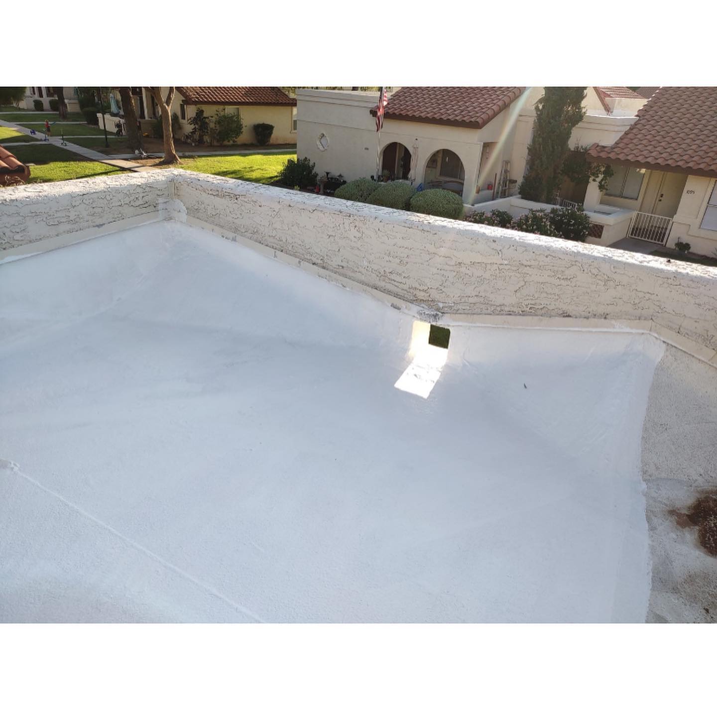White flat roof with small square drain, buildings in background.