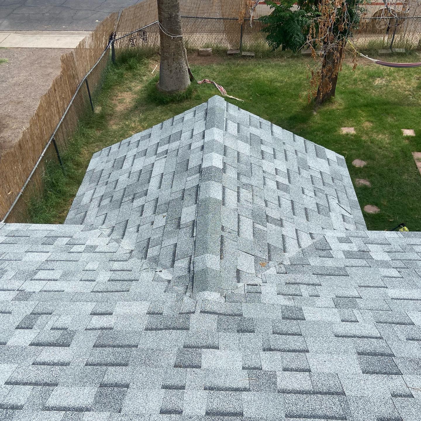 Overhead view of a roof covered in gray and white shingles, with a backyard visible in the background.