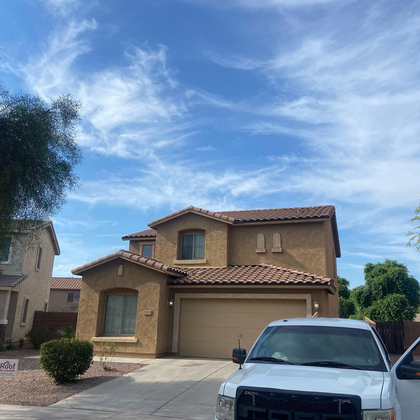Two-story stucco house with a garage and a white pickup truck parked in front; blue sky with clouds.