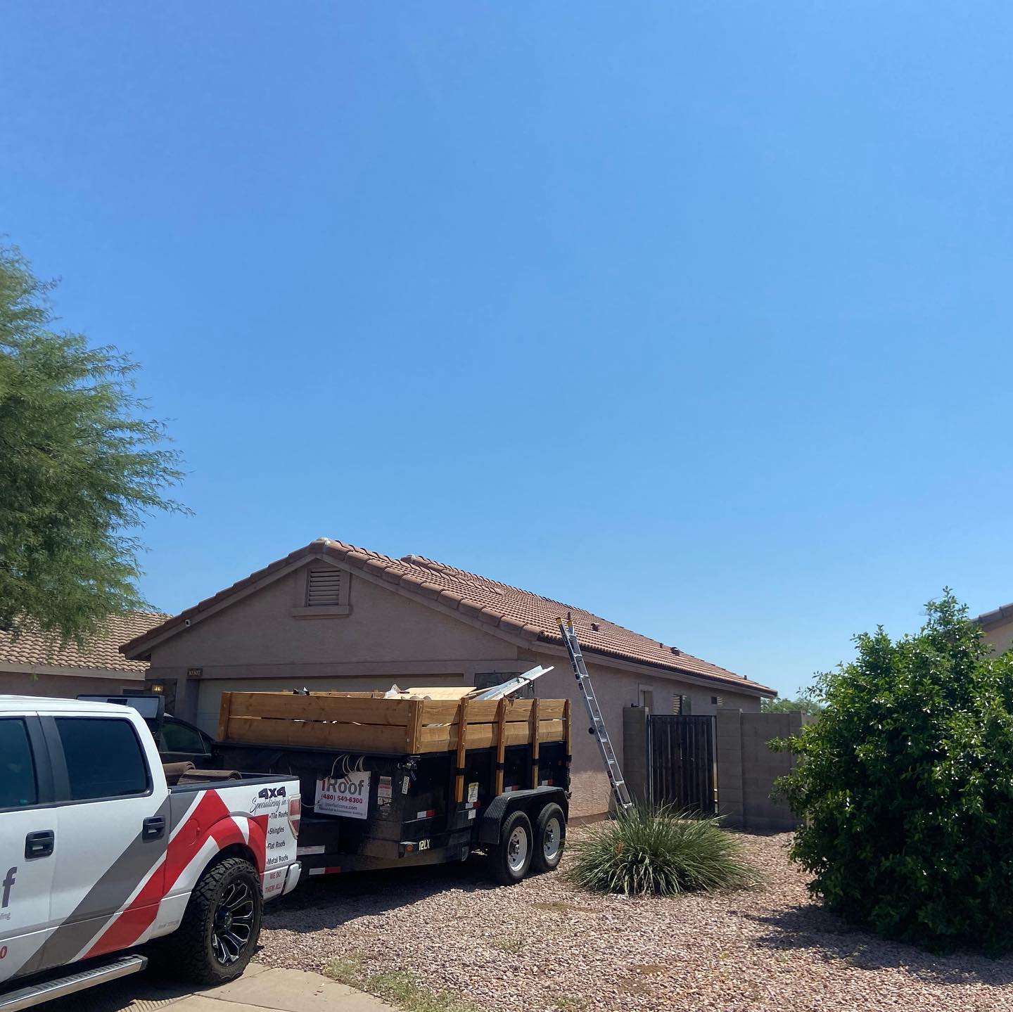 A truck and trailer with building materials parked in front of a house on a sunny day.