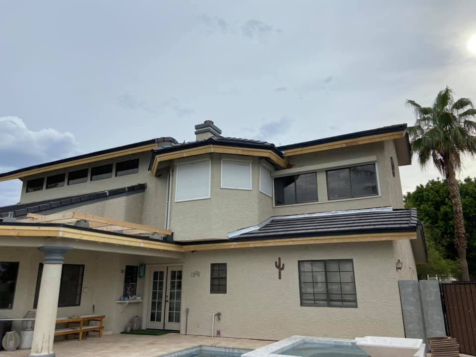 Two-story house with tan stucco exterior, dark roof, pool, and palm tree. Construction in progress.