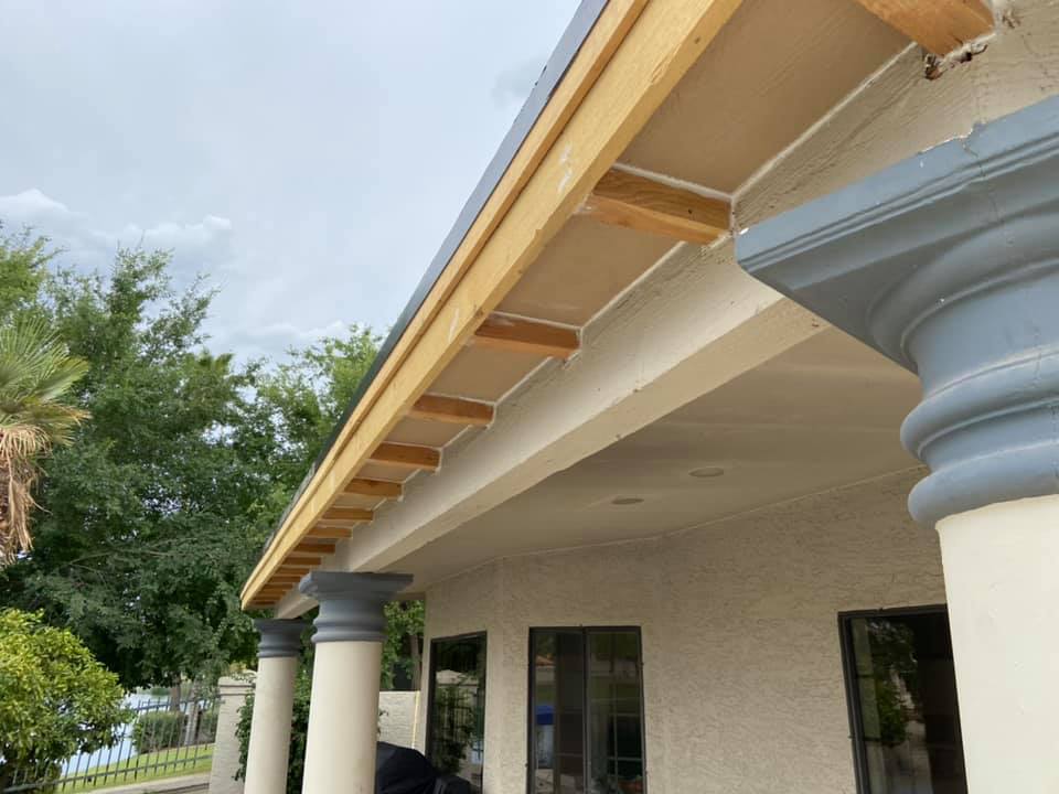 Construction on the eaves of a stucco building with columns. Wooden beams and new material visible.