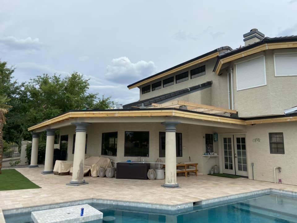 Backyard patio with columns, pool, and house under cloudy sky.