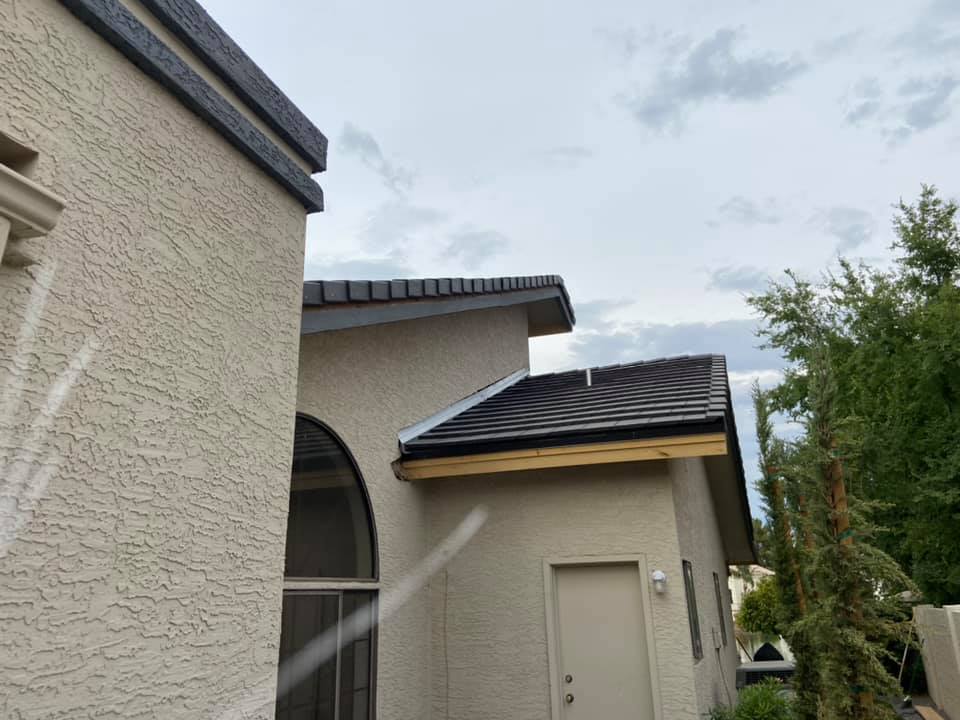Beige stucco buildings with dark roof tiles against a cloudy sky, trees on the right.