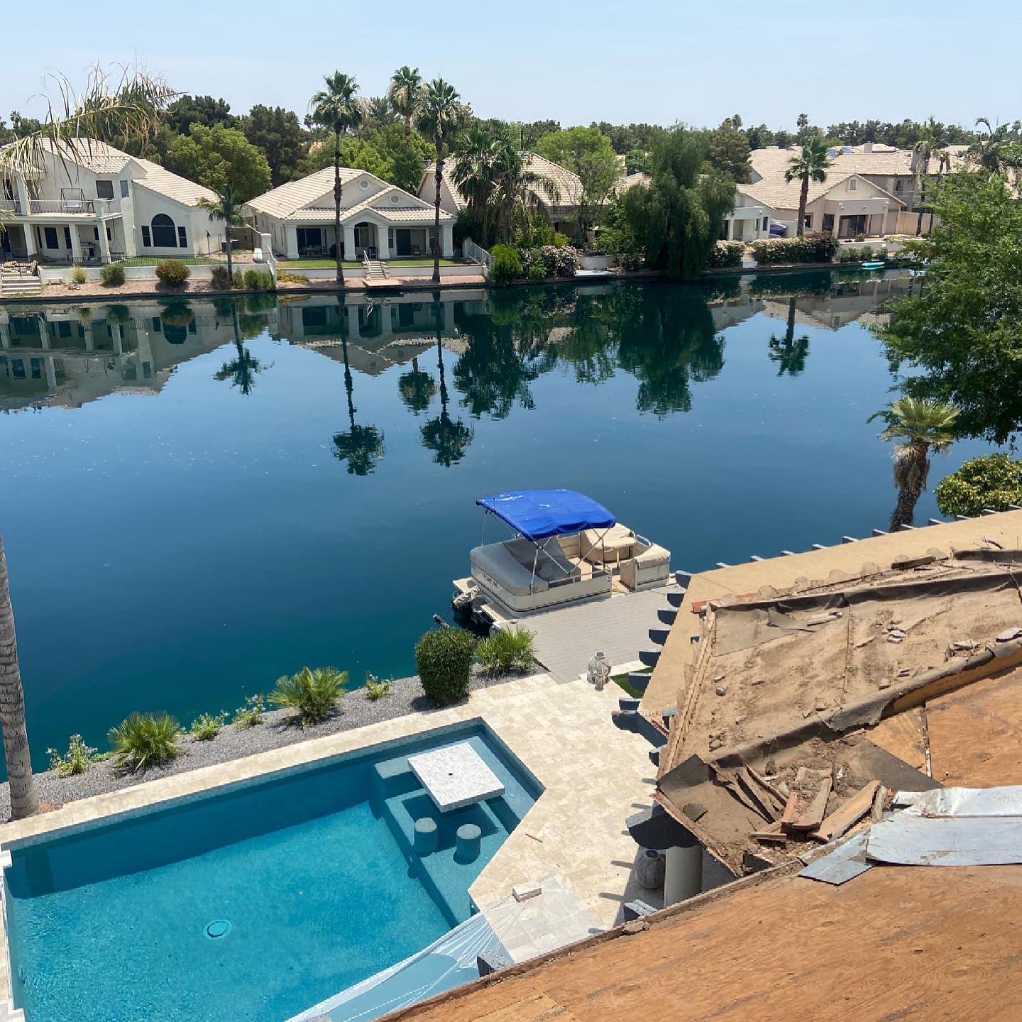 Lakeside view with blue pool and dock, houses and palm trees reflected in the water on a sunny day.