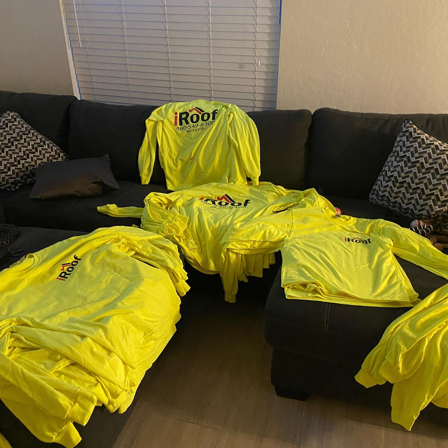 Yellow iRoof work shirts piled on a black couch, next to decorative pillows.