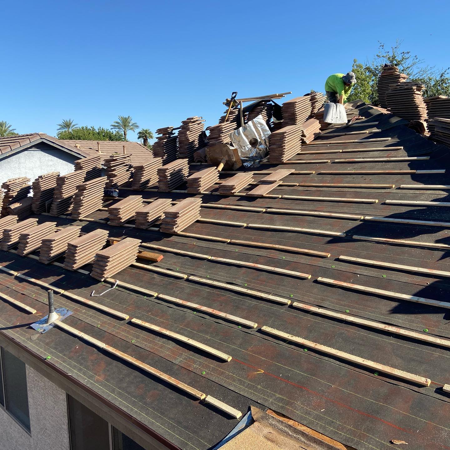 Roofers replacing clay tiles on a house roof. Tiles are stacked, worker in green vest.