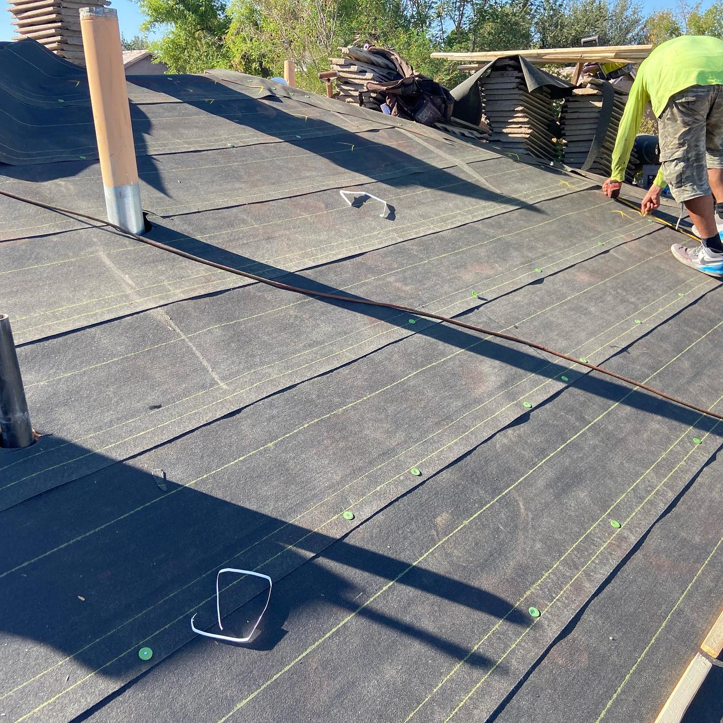 Roofer installing dark roofing material on a sloped roof in daylight.