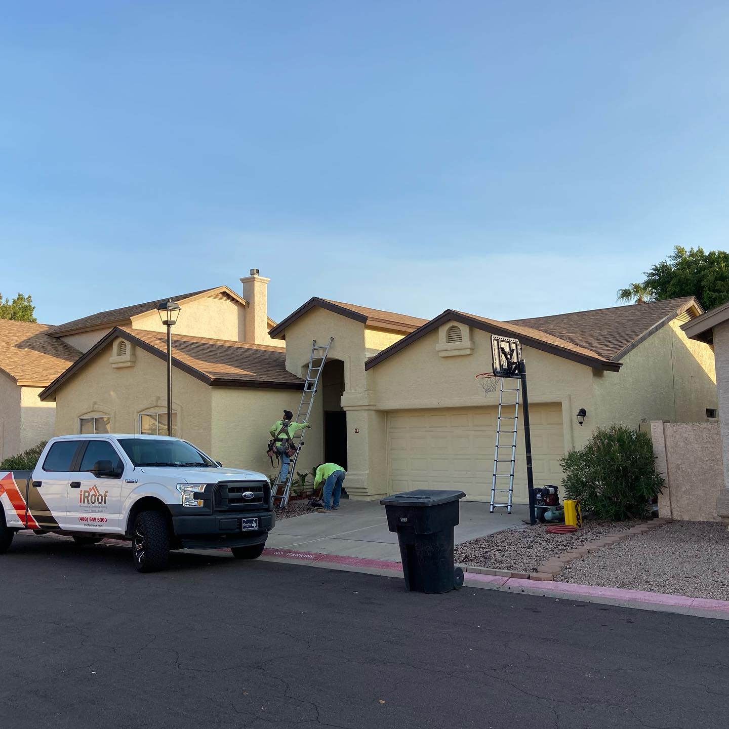 Workers on a ladder near a beige house, with a truck parked in the street.