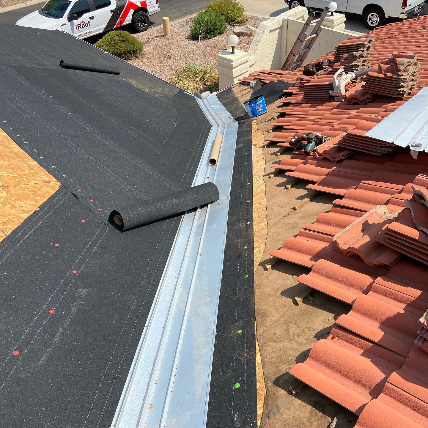 Roof under construction, showing underlayment, metal flashing, and clay tiles on a house.