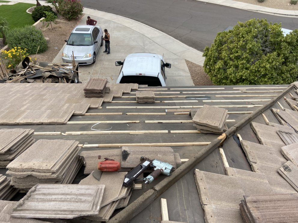 Roof repair in progress; workers on a roof, tools, stacked tiles, vehicles in driveway.