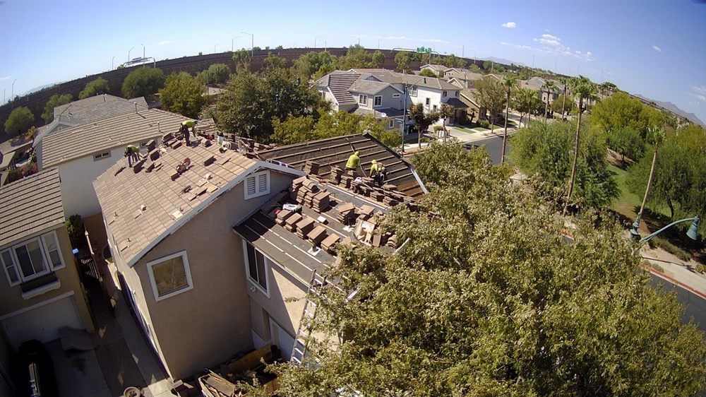 Rooftop being worked on with visible roof tiles, houses, and trees on a sunny day.