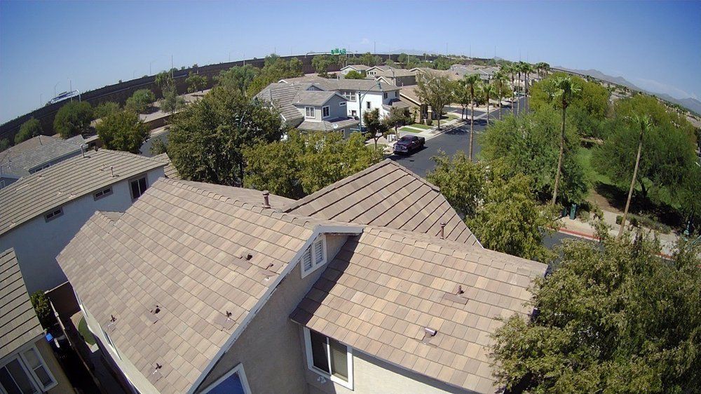 Overhead view of suburban homes, a street with a car, and green trees under a blue sky.