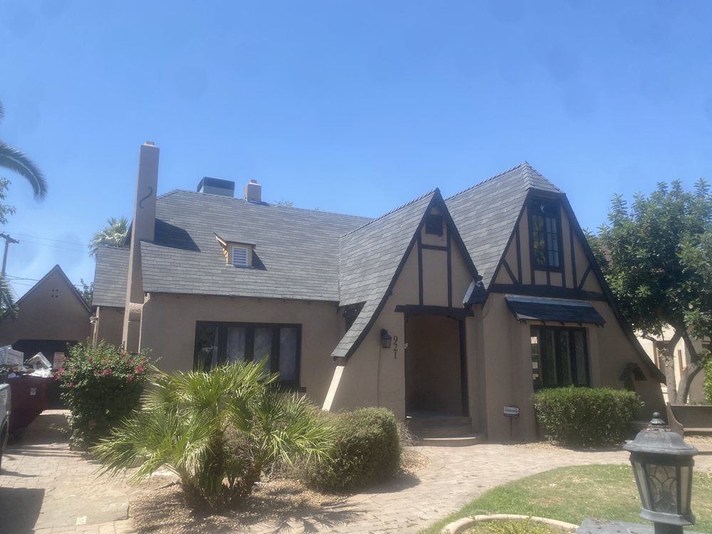 Tudor-style house with tan stucco, black accents, and dark gray roof under a blue sky.