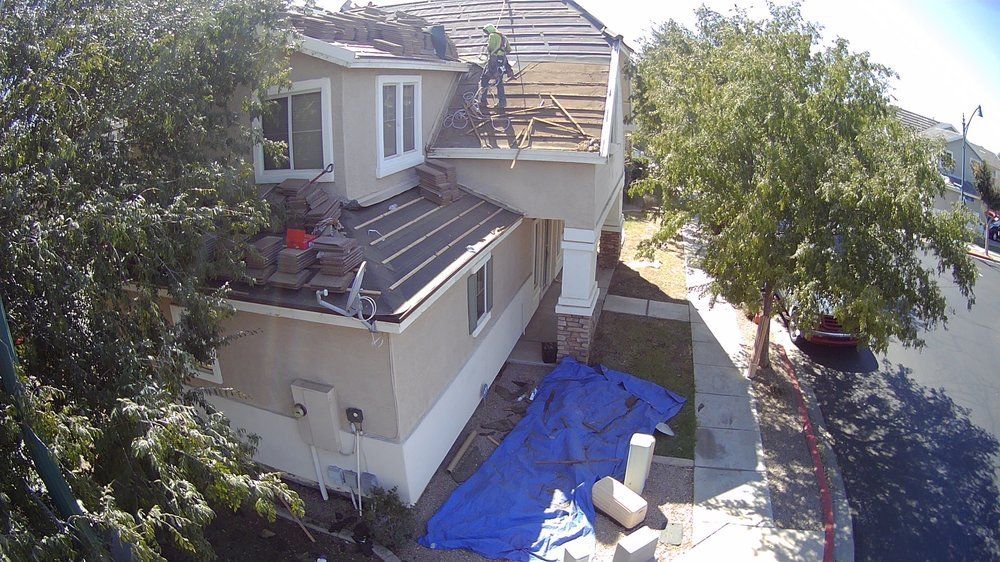 House with roof partially removed, tarp on the ground, workers on roof.