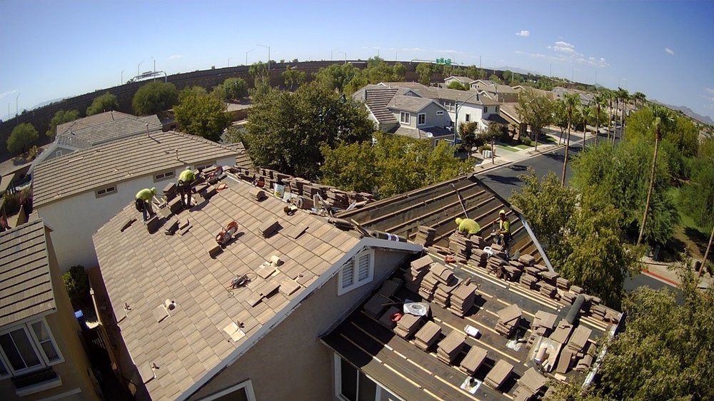 Roofers working on a tiled roof of a house in a suburban neighborhood.