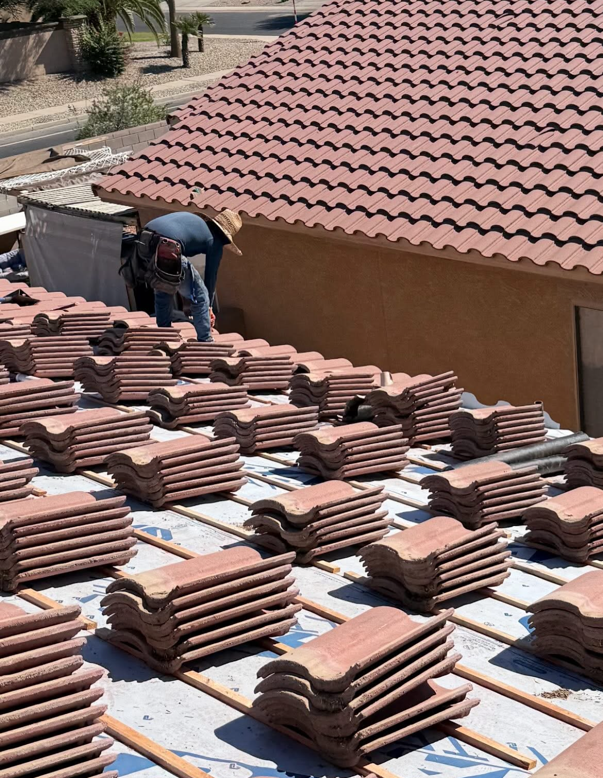 Roofer laying red clay tiles on a rooftop. Tiles stacked on the roof next to the worker.