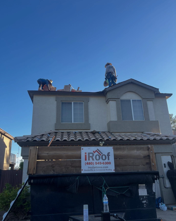Roofers working on a two-story house under a clear blue sky. A sign for iRoof is below the roof.