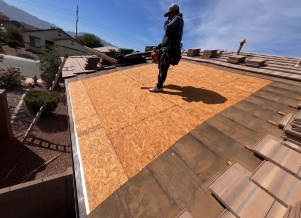Roofer on a partially tiled rooftop, standing on OSB.  Clear sky, residential setting.