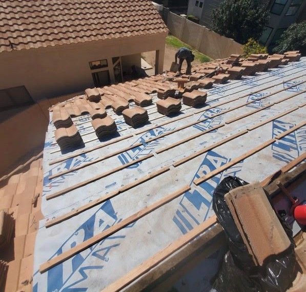 Roofer laying clay tiles on a house roof with blue underlayment and wood strips.