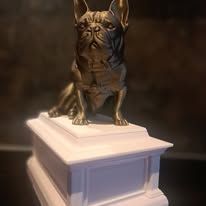 Een bronskleurig beeldje van een Franse bulldog staat op een rechthoekig, trapsgewijs wit voetstuk.