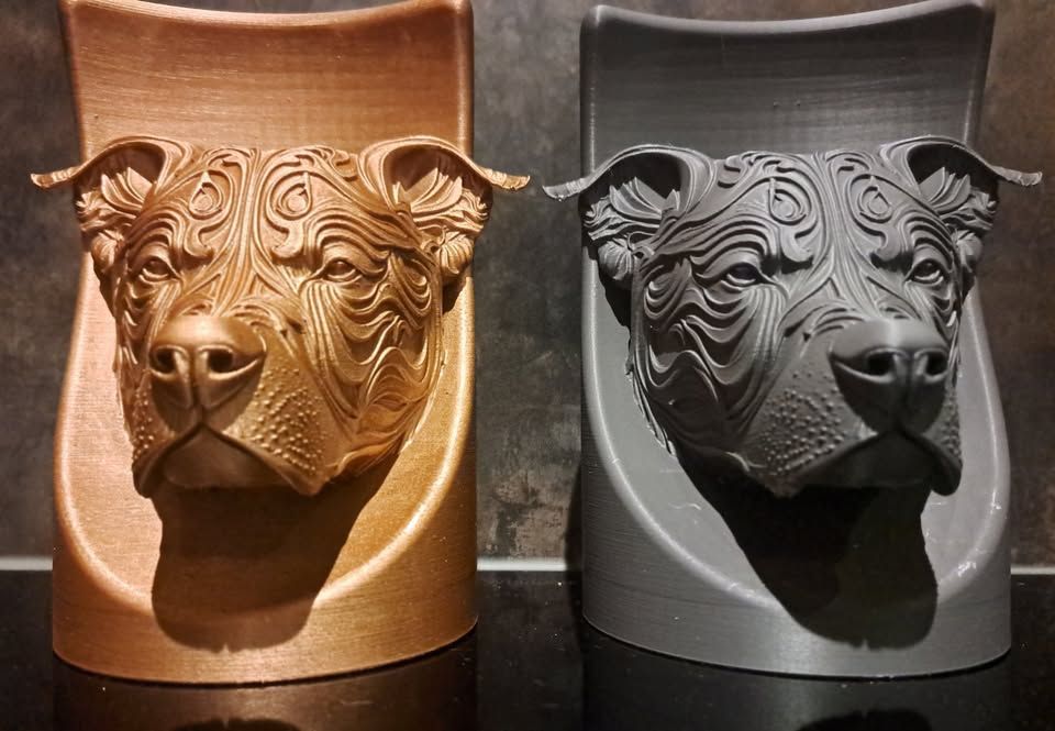 Twee 3D-geprinte hondensculpturen met ingewikkelde, wervelende patronen, een in metallic goud en een in matgrijs, staan ​​naast elkaar.