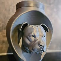 Een grijze, 3D-geprinte urn met de gebeeldhouwde kop van een pitbull in een afgerond, open frame.