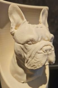 Een wit, 3D-geprint beeldje van een Franse bulldogkop, gemonteerd op een wandplaat.