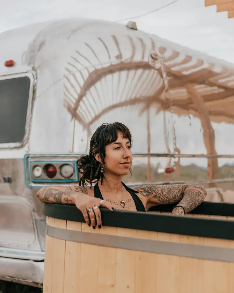 a woman is sitting in a wooden tub in front of an airstream .