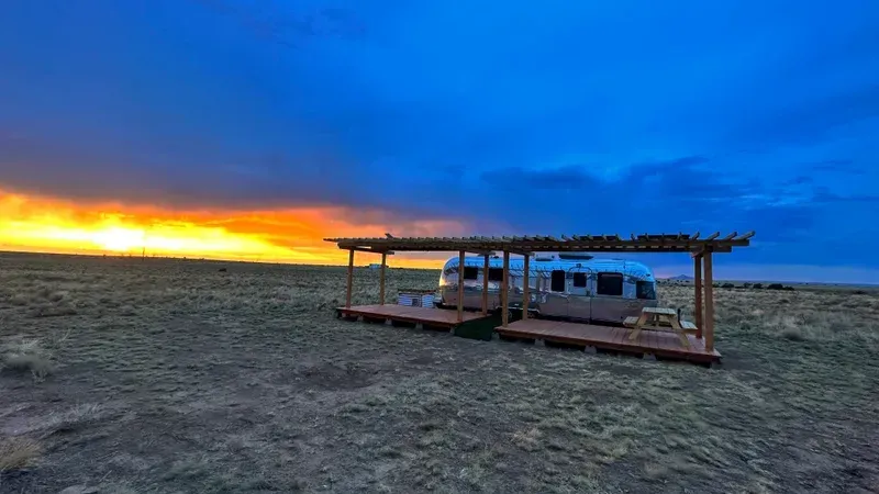 a rv is parked under a pergola in the middle of a desert at sunset .