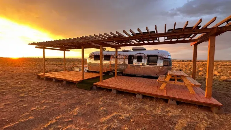 an airstream is parked under a pergola in the desert .